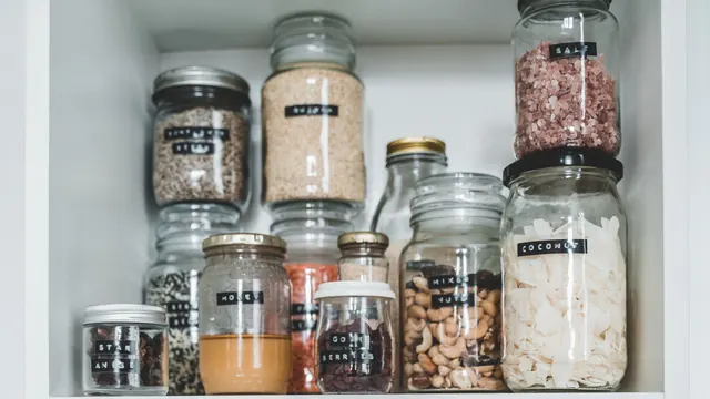 Labelled glass jars of nuts, spices and other ingredients on a white cupboard shelf