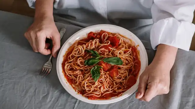 A plate of spaghetti with tomato sauce and basil on a grey tablecloth