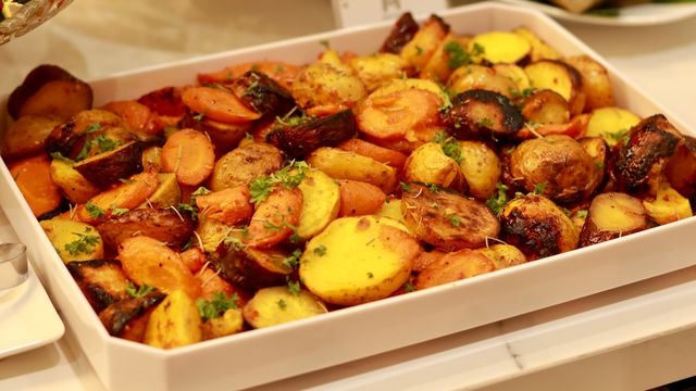 Roasted sliced potatoes and carrots seasoned with chopped fresh herbs in a white rectangular baking dish.