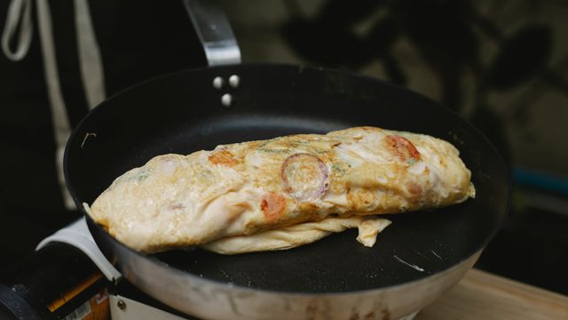 A folded omelette with visible vegetable filling cooking in a black frying pan.