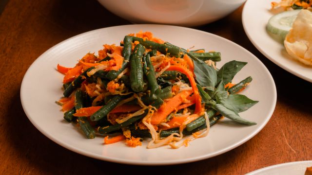 A seasoned green bean salad mixed with shredded carrots and bean sprouts on a white plate