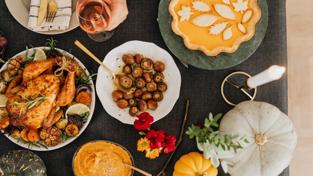 An overhead view of an autumn dinner table with roast chicken, mushrooms, a pie, pumpkins, and a lit candle.