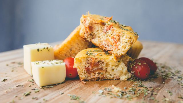 Savoury muffins cut open showing cheese and tomato filling, served with cheese cubes and cherry tomatoes on a wooden board